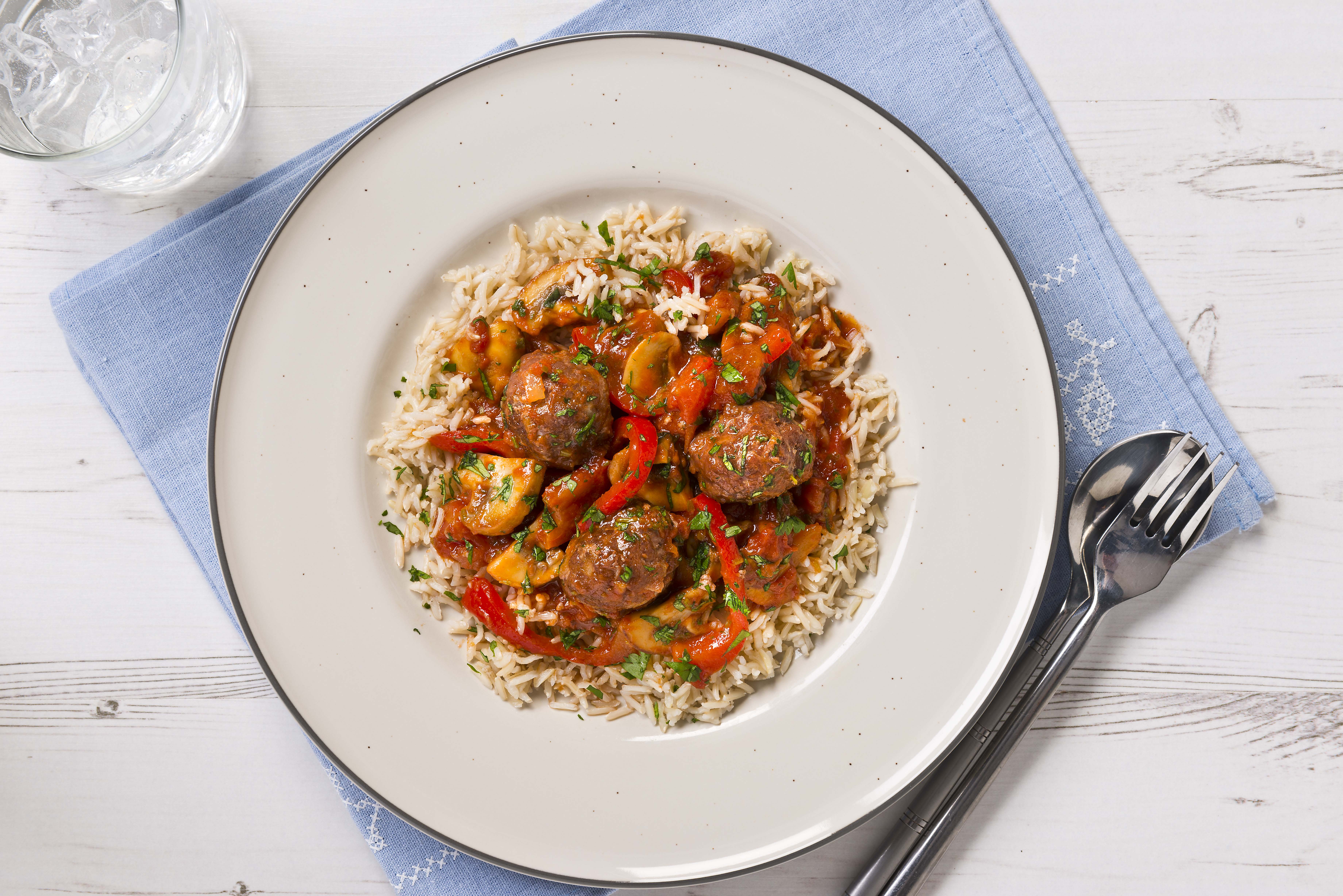 A plate with rice and beef meatballs in a tomato sauce.