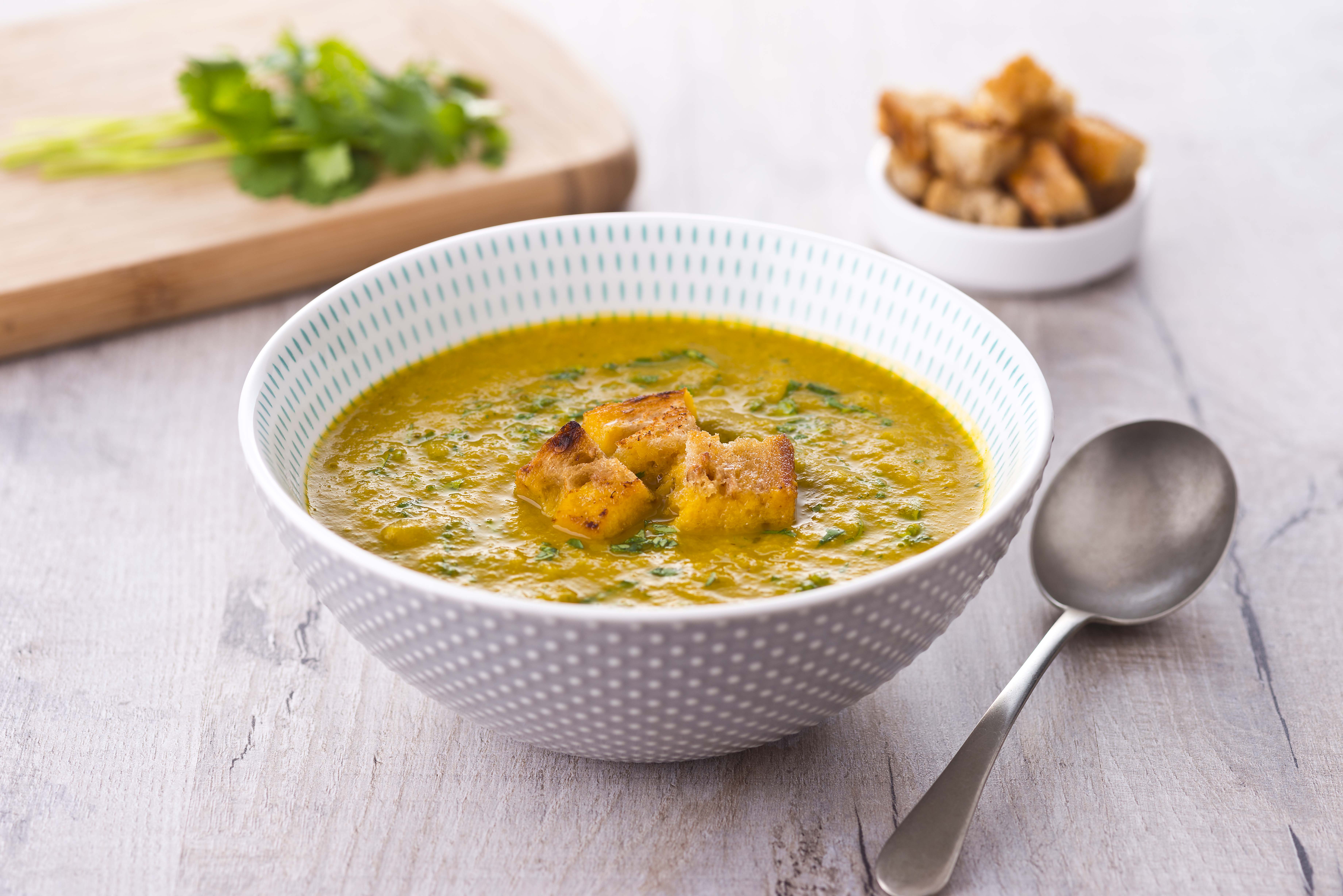 A bowl of carrot and orange soup with some croutons on the side