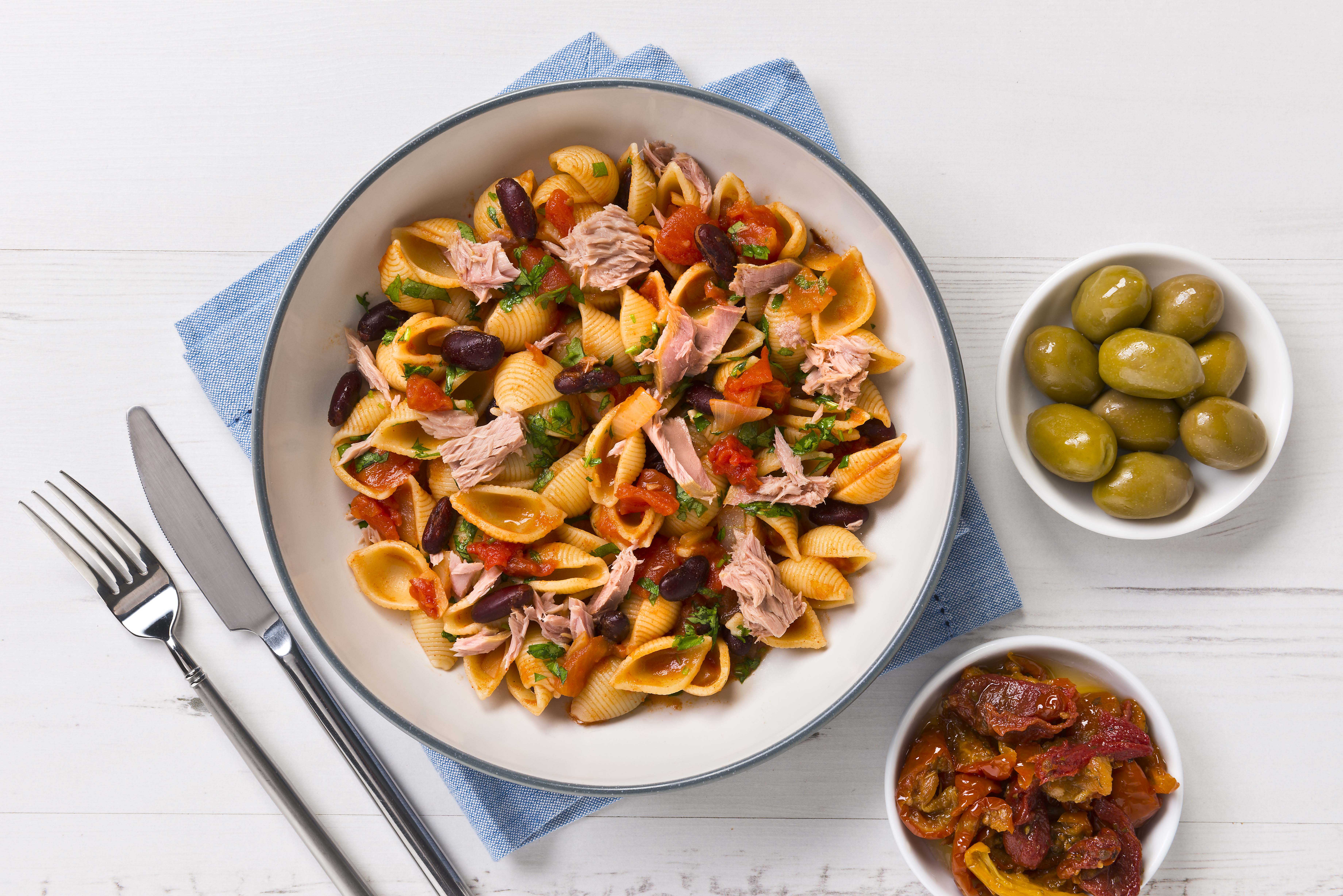 A serving of pasta with tuna and beans and olives on the side