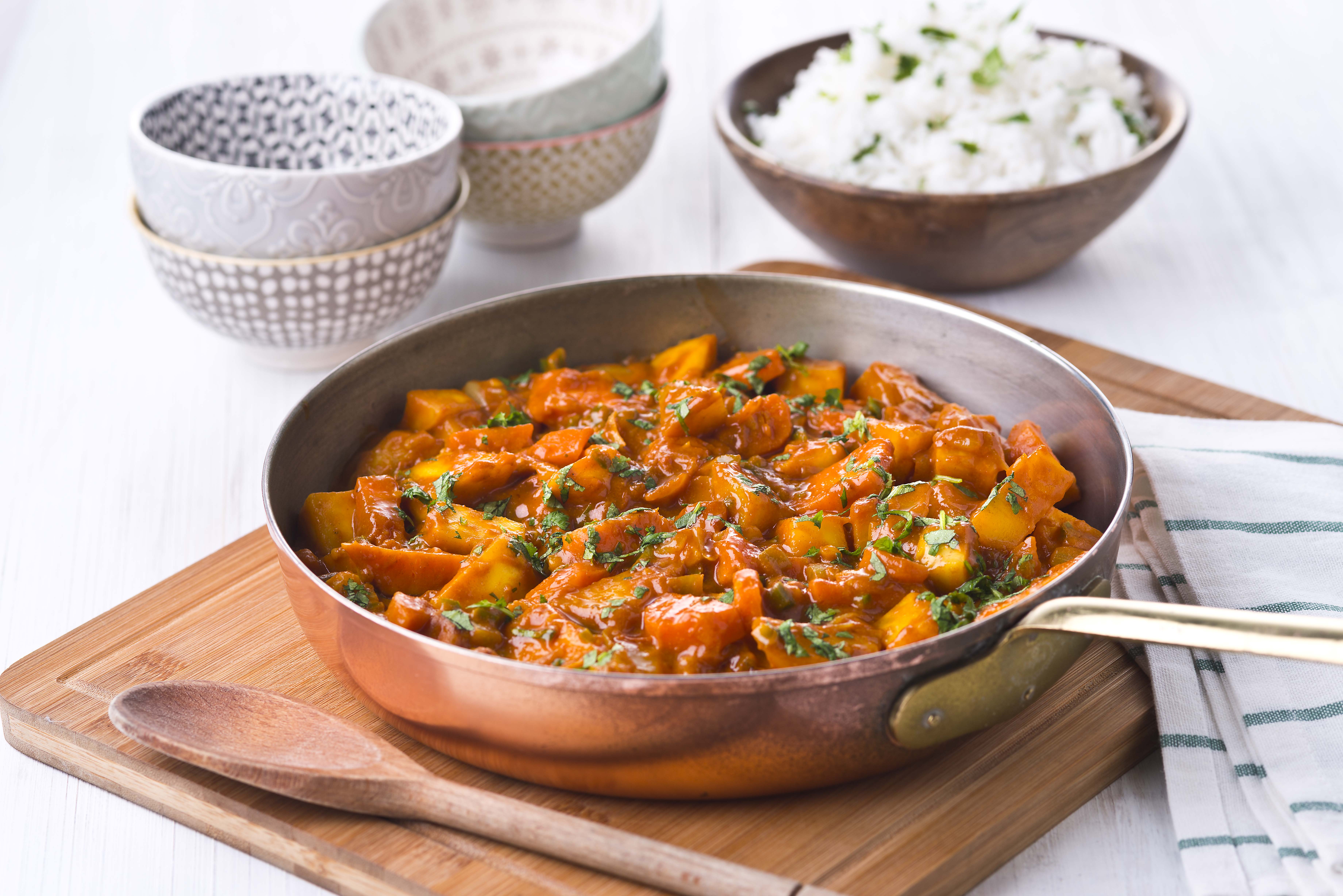 A bowl of root vegetable curry served with rice and sauces