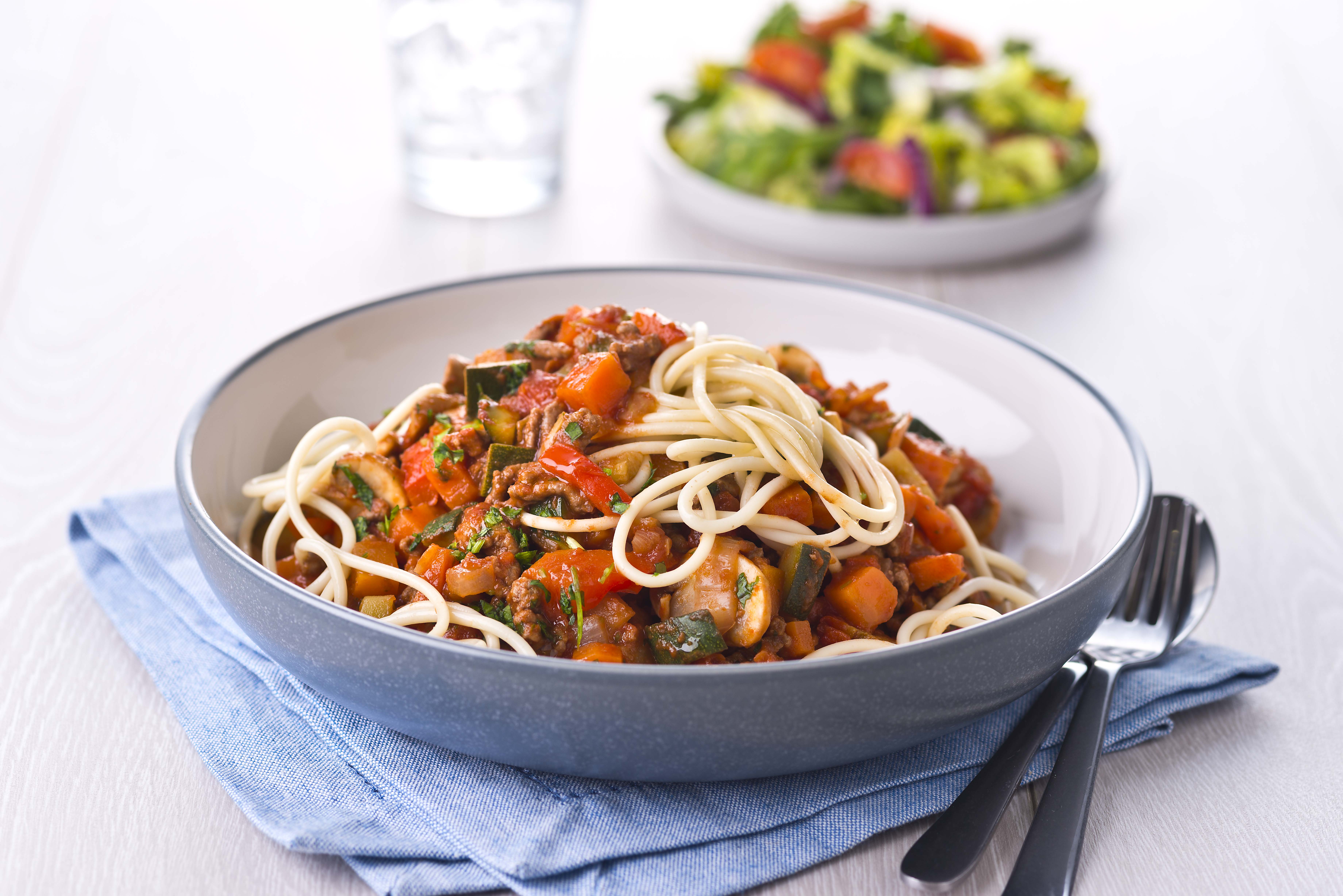 A dish of spaghetti bolognaise with a green salad side dish